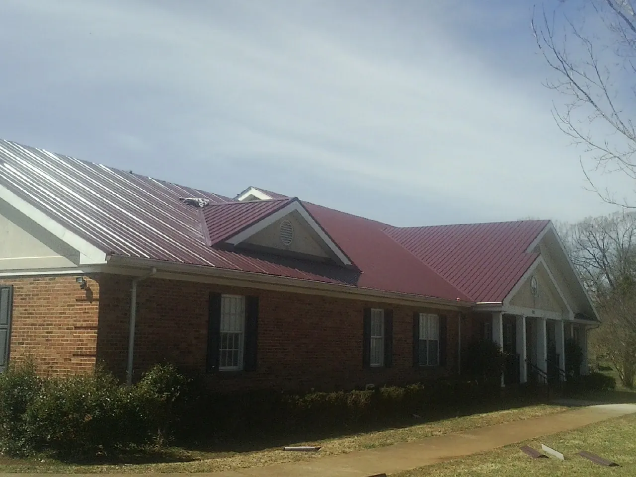 Red metal roof with gabled entries on a long brick building, from a Hail Damage Roof Repair job in Barnesville